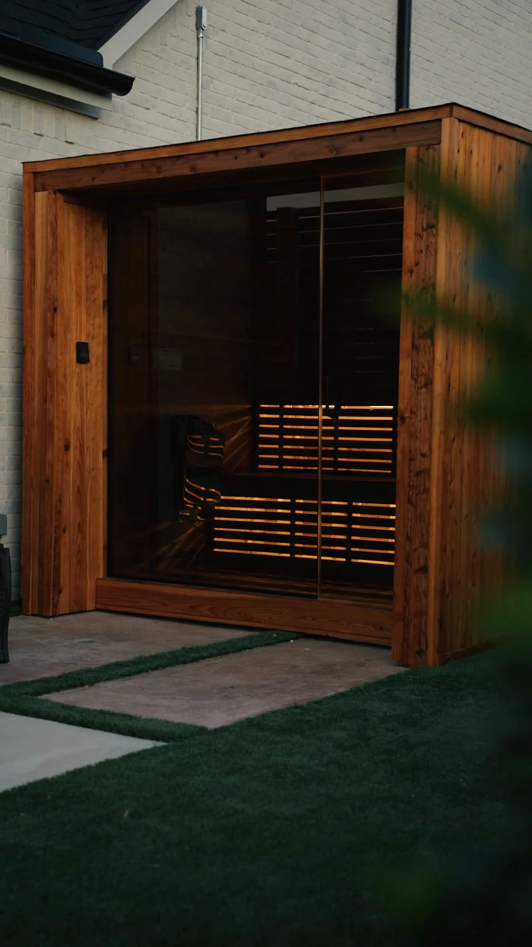 Cedar cube sauna with slat privacy screen on artificial turf at golden hour