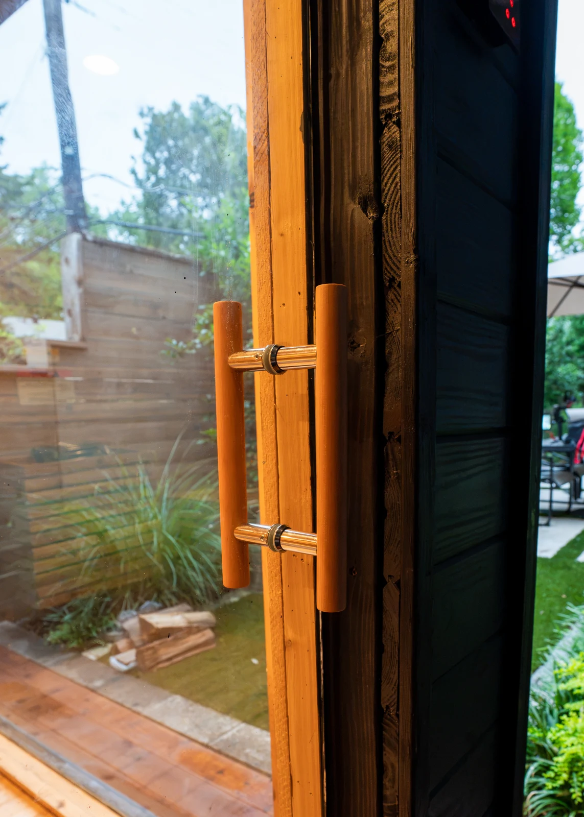 Handcrafted cedar door handle on glass sauna door with backyard beyond