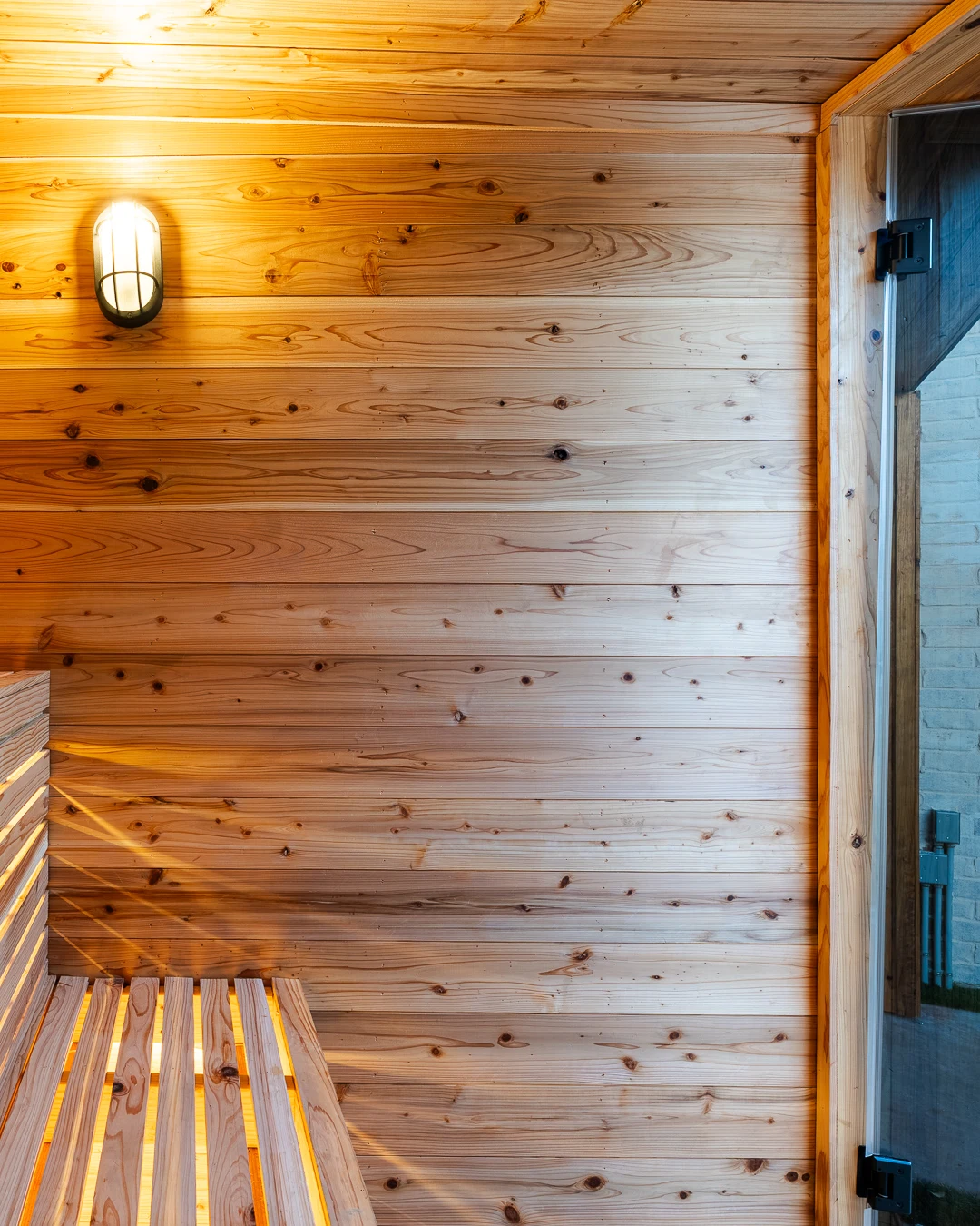 Glass door handle with bulkhead sconce glowing in cedar sauna