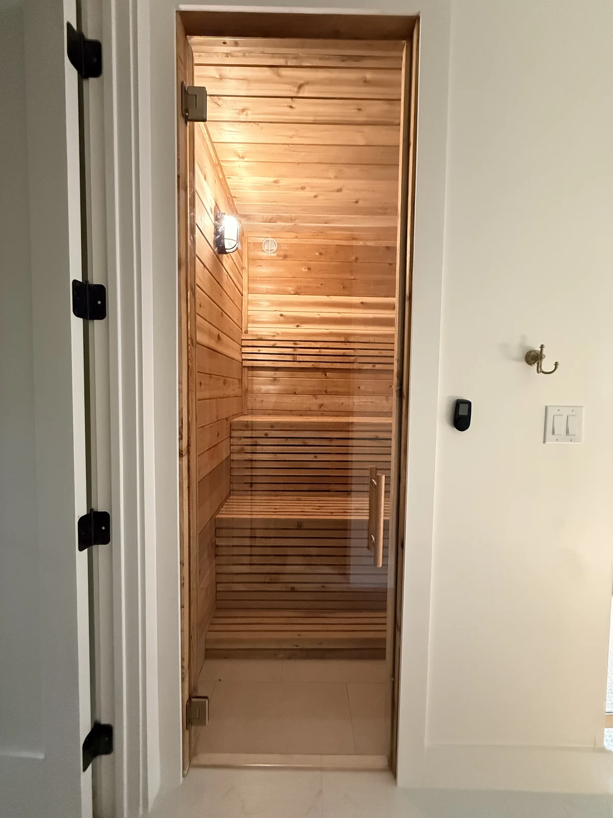 Indoor cedar sauna behind a narrow frameless glass door in a white master suite