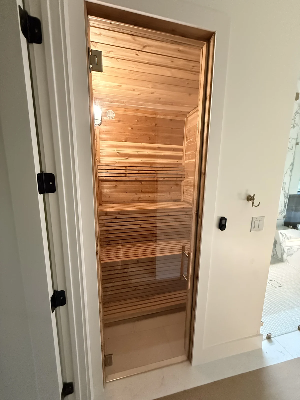 Indoor cedar sauna beside marble bathroom seen through glass door