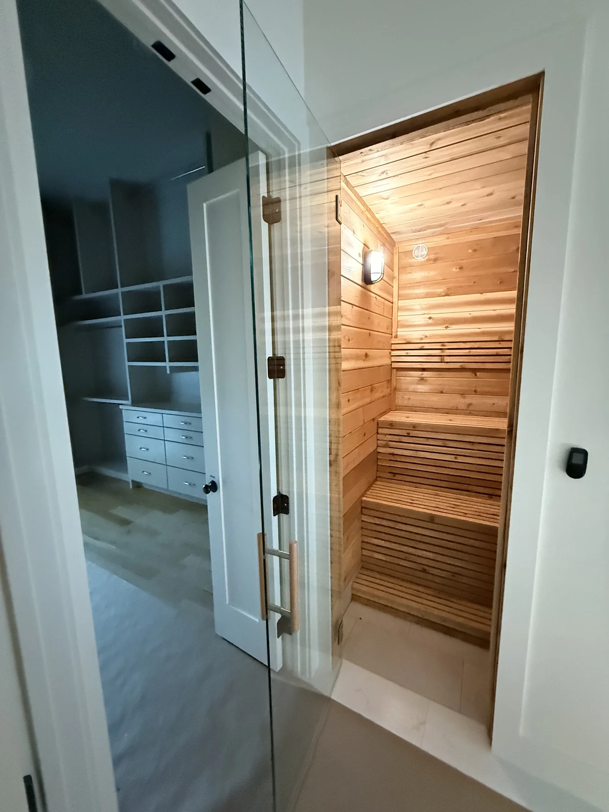 Glass sauna door opening into master suite with walk-in closet beyond