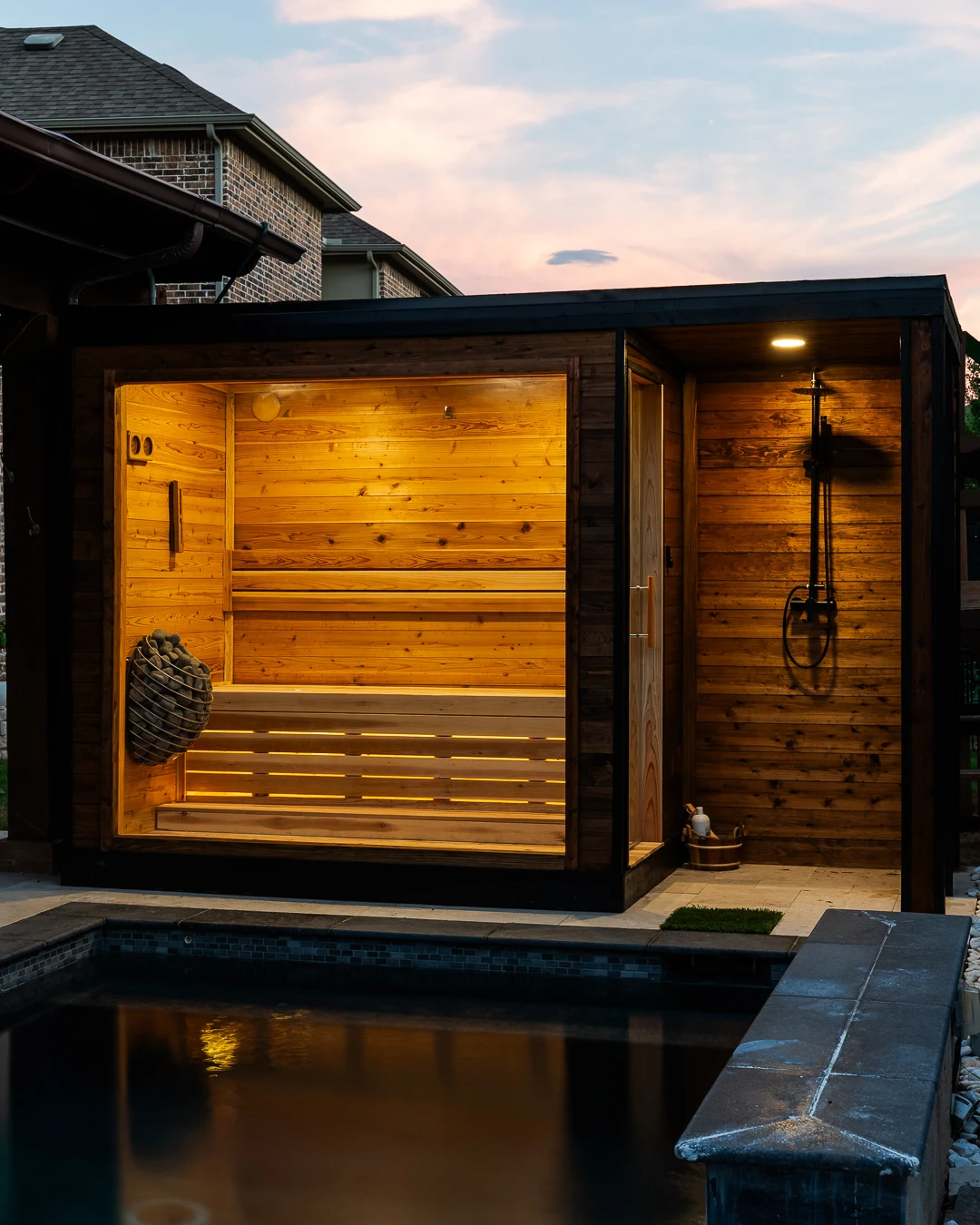 Poolside sauna with glass front and outdoor shower under a dusk sky