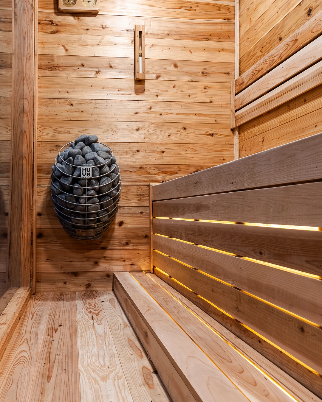 Wall-mounted HUUM Drop heater with stones above LED-backlit cedar benches